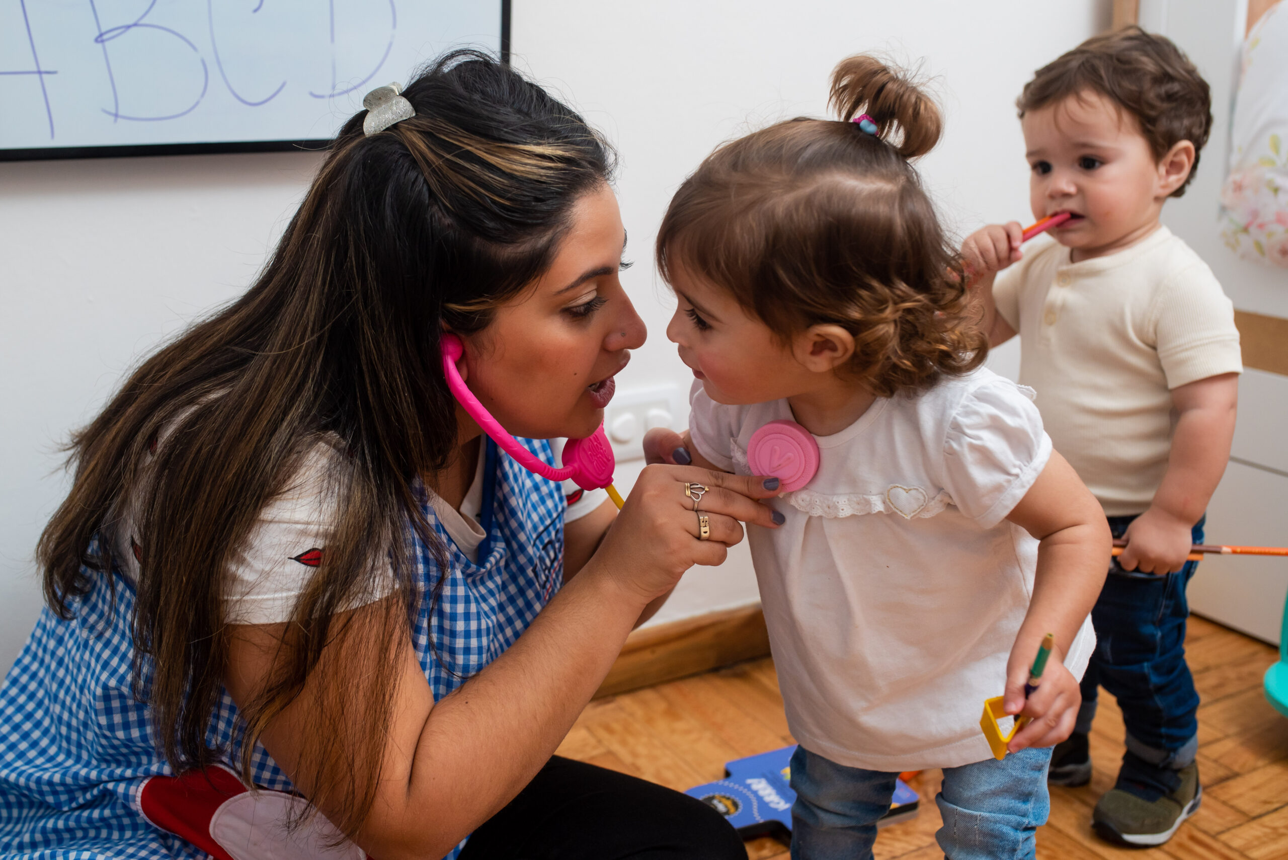 Happy children playing or studying in classroom with young kindergarten teacher