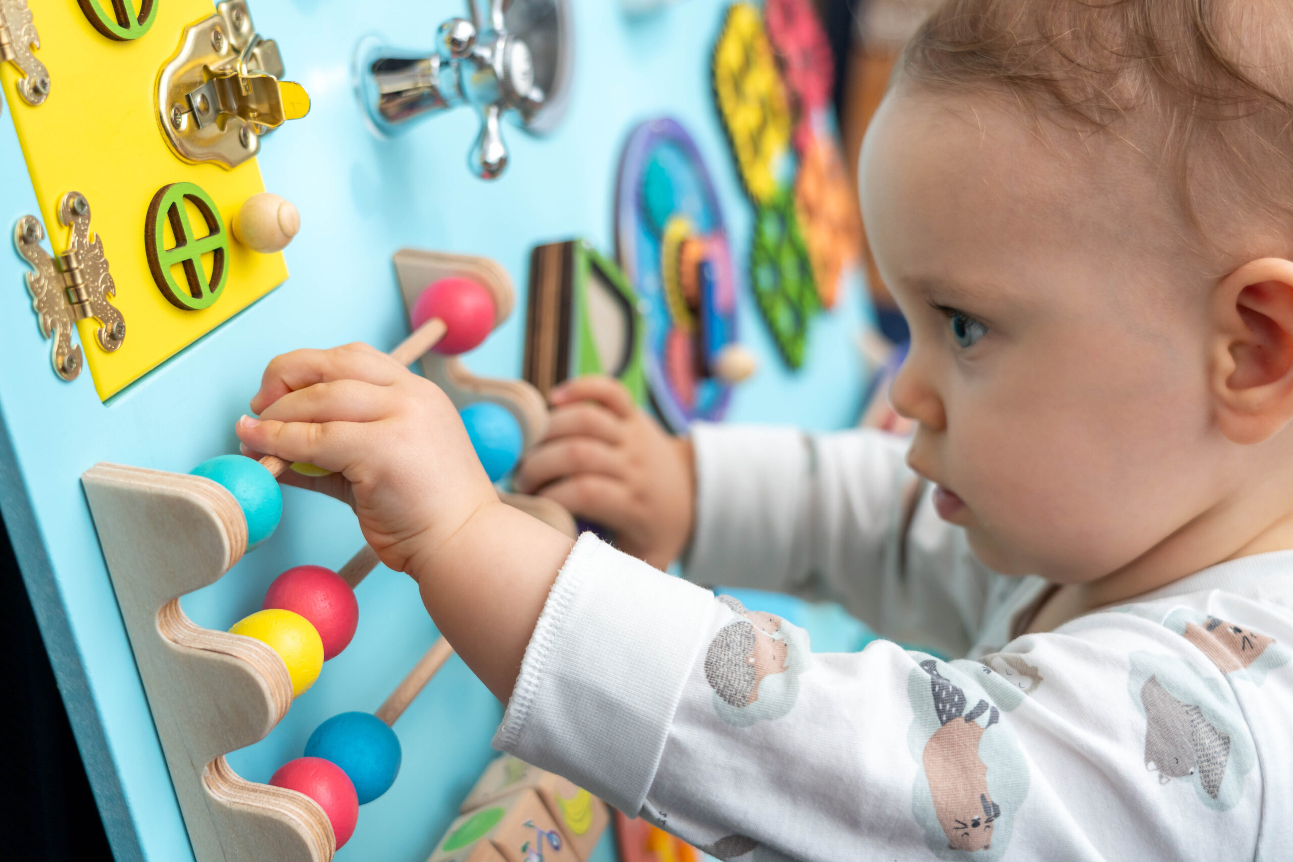 A baby moves round colored wooden elements on a busy board.